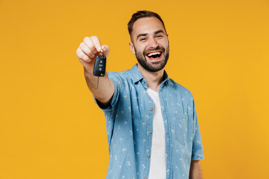 Young smiling happy caucasian man 20s wearing blue shirt white t-shirt hold give car key fob keyless system look camera isolated on plain yellow background studio portrait. People lifestyle concept.