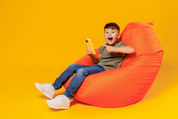 Full body little small happy boy 6-7 years old wear green t-shirt sit in bag chair hold use point...