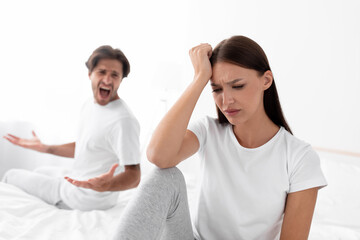 Unhappy upset caucasian millennial wife ignores screaming husband, lady sits in bed in bedroom interior