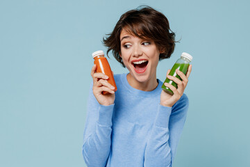 Young excited woman 20s in casual sweater hold pressed juice green orange vegetable smoothie as...