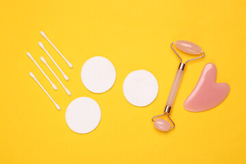 Face roller and gua sha stone massager, cotton pads and sticks on gray background. Top view