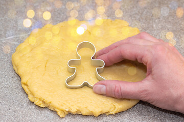 The chef's hand is cutting out the shape of gingerbread men from raw rolled dough on a background with yellow bokeh