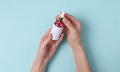 Female hands hold Facial serum bottle on blue background