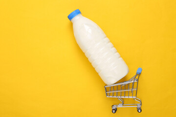 Mini shopping cart with milk bottle on yellow background