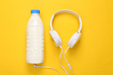 Milk bottle with headphones on yellow background. Top view