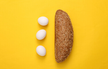 Loaf of cereal bread with chicken eggs on yellow background