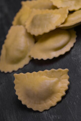 Tasty raw ravioli with flour and spinach on dark background, process of making italian ravioli