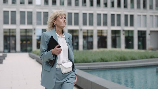 Mature woman in suit walking with documents folder in hands