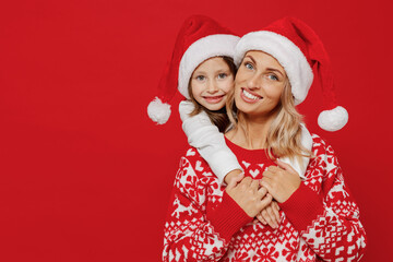Young woman in sweater hat have fun with child baby girl 6-7 years old Mommy little kid daughter cuddle hugging look camera isolated on plain red color background studio New Year love family concept
