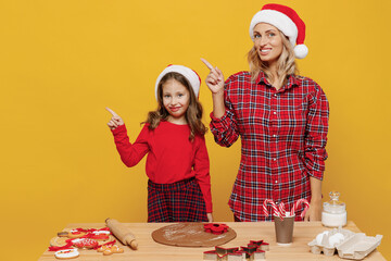 Two woman mother fun child baby girl in red Christmas hat isolated on plain yellow wall background studio. Mom little kid cook ginger cookie at kitchen table home. Happy New Year 2022 holiday concept