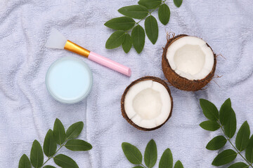 Natural cosmetology concept. Jar of cream and coconut, green leaves on a towel