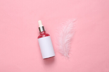 Facial serum bottle with soft feather on pink background. Beauty layout