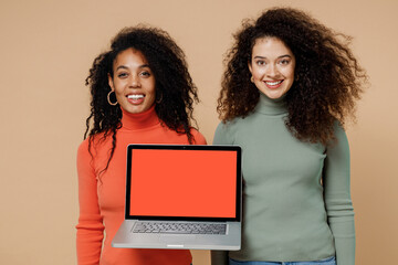 Obraz na płótnie Canvas Two happy young curly black women friends 20s wear casual shirts clothes hold use work on laptop pc computer with blank screen workspace area isolated on plain pastel beige background studio portrait.