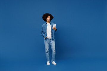 Full body fun young smiling happy black woman in casual clothes shirt white t-shirt hold in hand use mobile cell phone isolated on plain dark blue background studio portrait. People lifestyle concept.