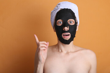 I have an idea. Beautiful woman in a cleansing black mask with a towel on her head on an orange background