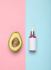 Bottle of face serum and avocado on pink blue background. Top view