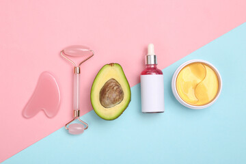 Naklejka premium Facial massage roller, serum bottle, patches, avocado on blue pink background. Cosmetic flat lay. Top view
