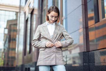 Young stylish business woman buttons a jacket button in the city.