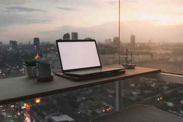 Laptop on wooden desk at the balcony with evening sunset city view.
