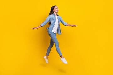 Full body profile photo of mature brown hair cool lady run wear jeans shirt sneakers isolated on yellow color background