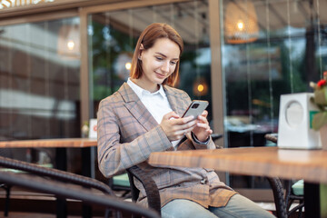 Young woman using phone while sitting at a table in an outdoor cafe