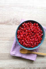 Bowl of fresh pomegranate seeds on wooden table. Top view.