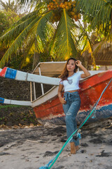 Young woman with red fishing boat dressed in blue jeans and white t-shirt posing on the beach. 