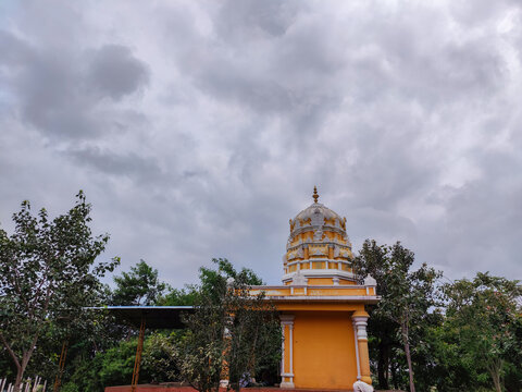 Stock photo of Beautiful lord shiva temple painted with light orange and white color on intricate carvings of god and goddess, temple surrounded by green trees. Picture captured at gulbarga India.