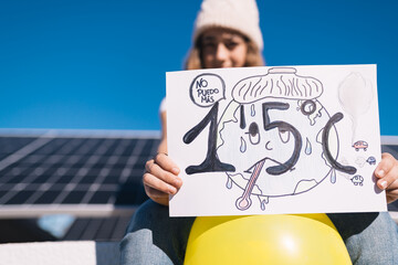 Teenage girl protests next to solar panels with a painted sign calling for preventing the earth's...