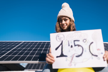 Teenage girl protests next to solar panels with a painted sign calling for preventing the earth's...
