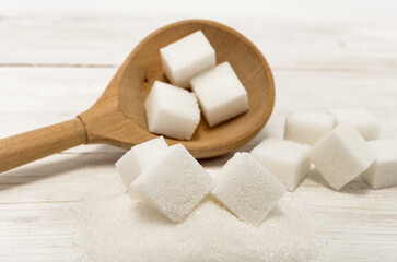 Refined sugar. Sugar lumps are scattered on a wooden surface, table and spoon