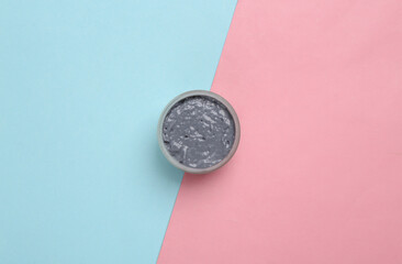 Jar of black clay on blue-pink pastel background. Cosmetic products. Beauty concept. Minimalism