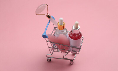 Mini shopping cart with face skin care products on pink background