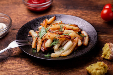 Fried potatoes on a plate with herbs on a wooden background. Ketchup, mayonnaise and bread lie side by side.