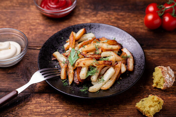 Fried potatoes on a plate with herbs on a wooden background. Ketchup, mayonnaise and bread lie side by side.