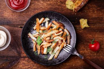 Fried potatoes on a plate with herbs on a wooden background. Ketchup, mayonnaise and bread lie side by side.