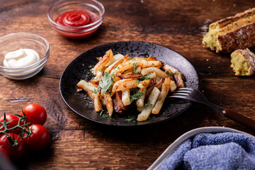 Delicious fried chopped potatoes with ketchup, mayonnaise and herbs on a wooden background.