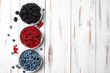 Fresh assorted berries - blueberries, blackberries and red currants in a plate on a white wooden background. Place for your text.