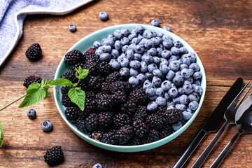 blueberries and blackberries on a plate on a dark wooden background with cutlery. The concept of vegetarianism, healthy food.