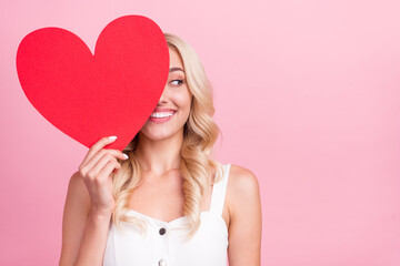 Photo of shiny pretty young lady wear white overall smiling large red heart close eye looking empty space isolated pink color background