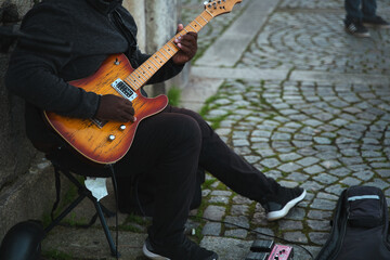 Unrecognisable african man sitting on a chair in the street playing the electric guitar.