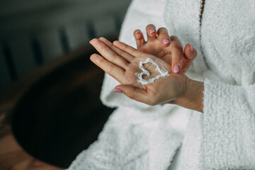 A woman in a white terry dressing gown at home in the bathroom painted a heart with white cream on her palm