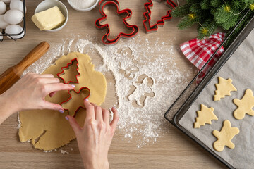 Woman Cutting Christmas gingerbread cookies. Making Christmas Cookies with traditional gingerbread cookies ingredients. Christmas Gingerbread man and fir trees on pan. Top view. - Powered by Adobe