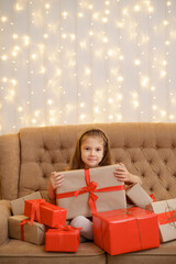 Beautiful girl among presents, enjoying the moment at home sitting o sofa surrounded by gift boxes