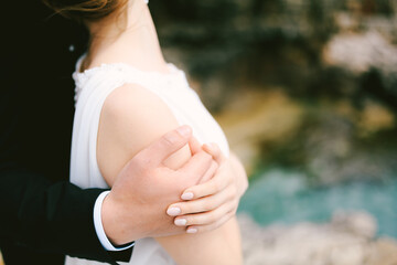 Fototapeta na wymiar Groom's hand hugs the shoulder of bride in a white dress. Close-up