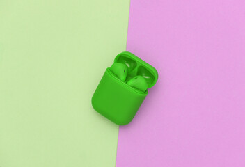 Green wireless headphones with charging case on pink green pastel background. Top view