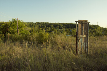 An old wooden door standing in the middle of the road among trees and bushes on a clear cloudless...