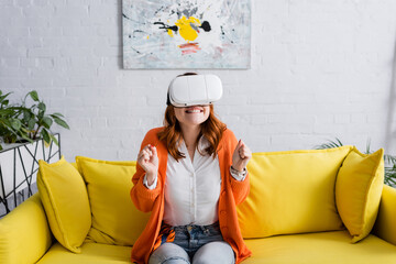 excited woman with clenched fists gaming in vr headset on sofa at home - Powered by Adobe
