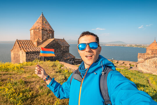 Man with armenian flag takes selfie photo against the background of Sevanavank monastery at the Sevan lake. Vacation and patriotism concept
