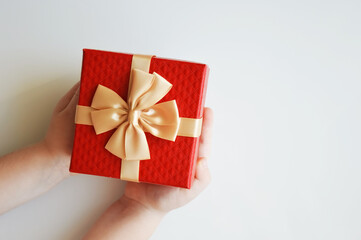 The child holds a red box with a golden bow for a gift on a white background. Decoration for winter holidays, Christmas and New Year.